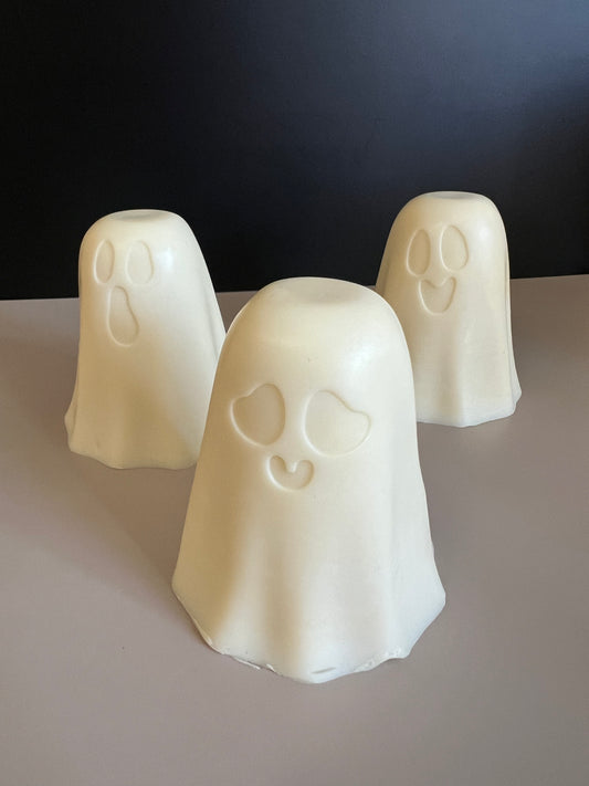 Three ghost-shaped white soaps with cute face details, arranged on a light gray surface against a dark background.