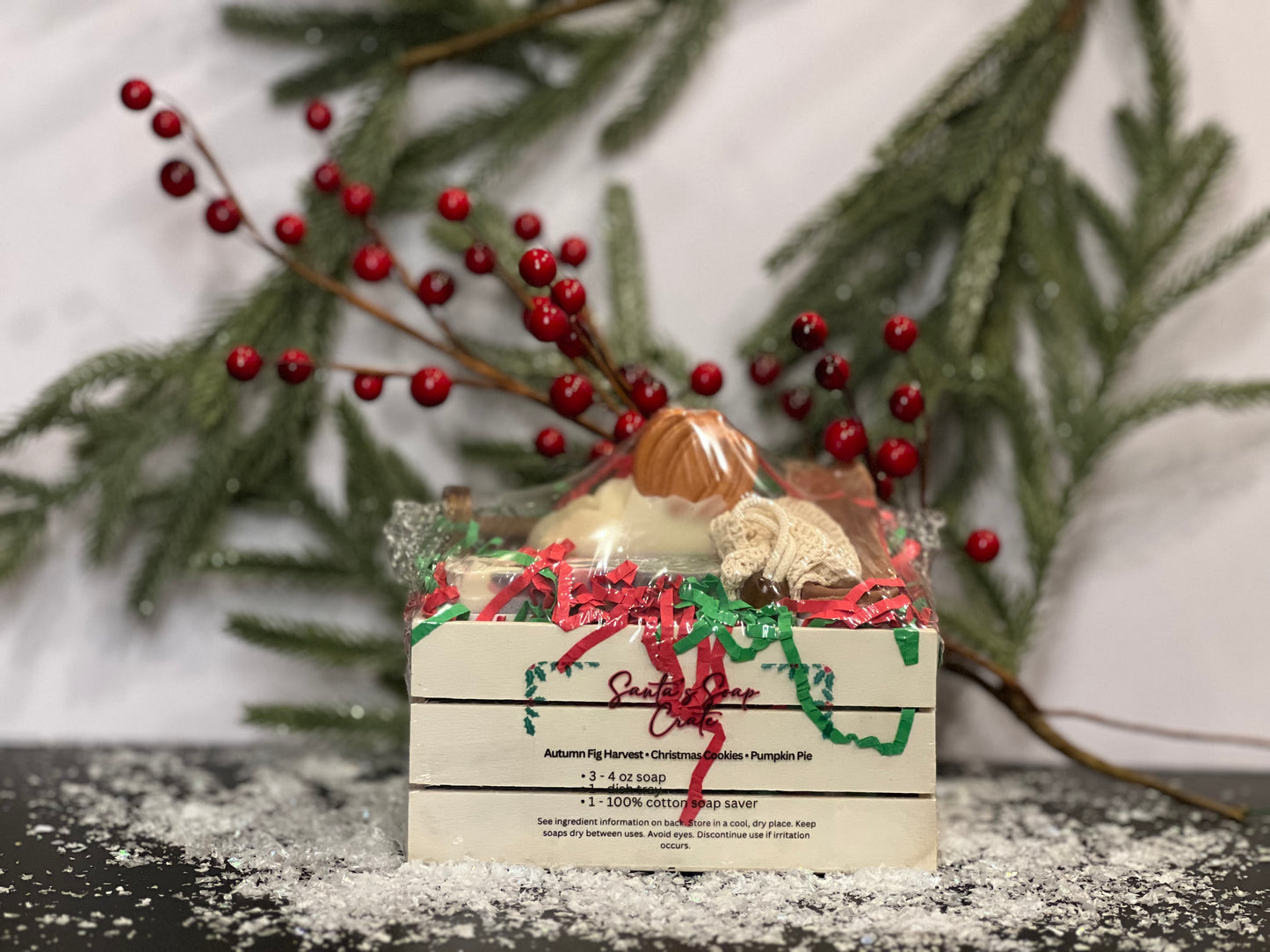 Soap in a small crate with Fall and Christmas designs and scents, with a white background, berries, tree foliage and snow decorations. 
