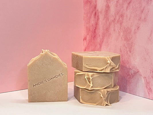 Three bars of a muted pink/beige soap stacked and one standing face forward on a white surface with 'Ande's Dandies' branding on a pink marble background