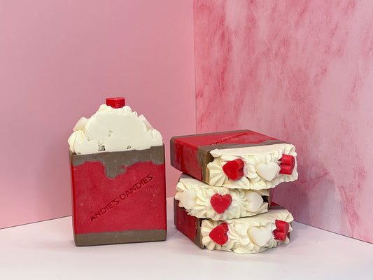 Stack of 3 brown red and white "chocolate covered strawberry with frosting" themed soap bars with one forward facing with small red and white hearts and biodegradable glitter on top and "Andie's Dandies" branding, on a white surface with a pink marble background