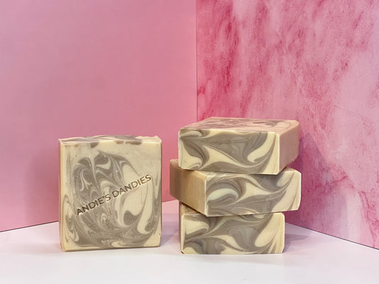 Three bars of brown and beige marbled soap stacked and one standing face forward on a white surface with 'Andie's Dandies' branding on a pink marble background