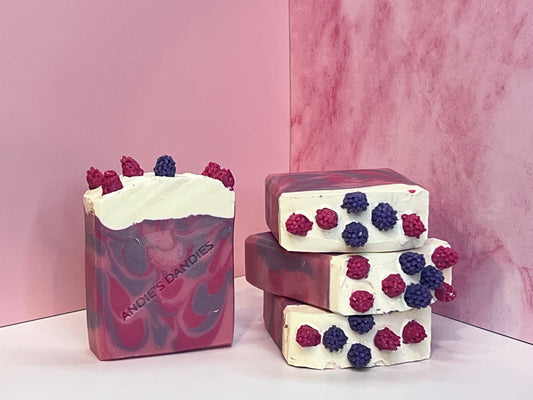 Stack of 3 pink and purple marbled soap bars with one forward facing with pink and purple berry toppings and "Andie's Dandies" branding on a white surface with a pink marble background