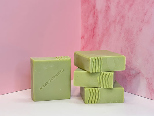 Three bars of green soap stacked and one standing face forward on a white surface with 'Andie's Dandies' branding on a pink marble background